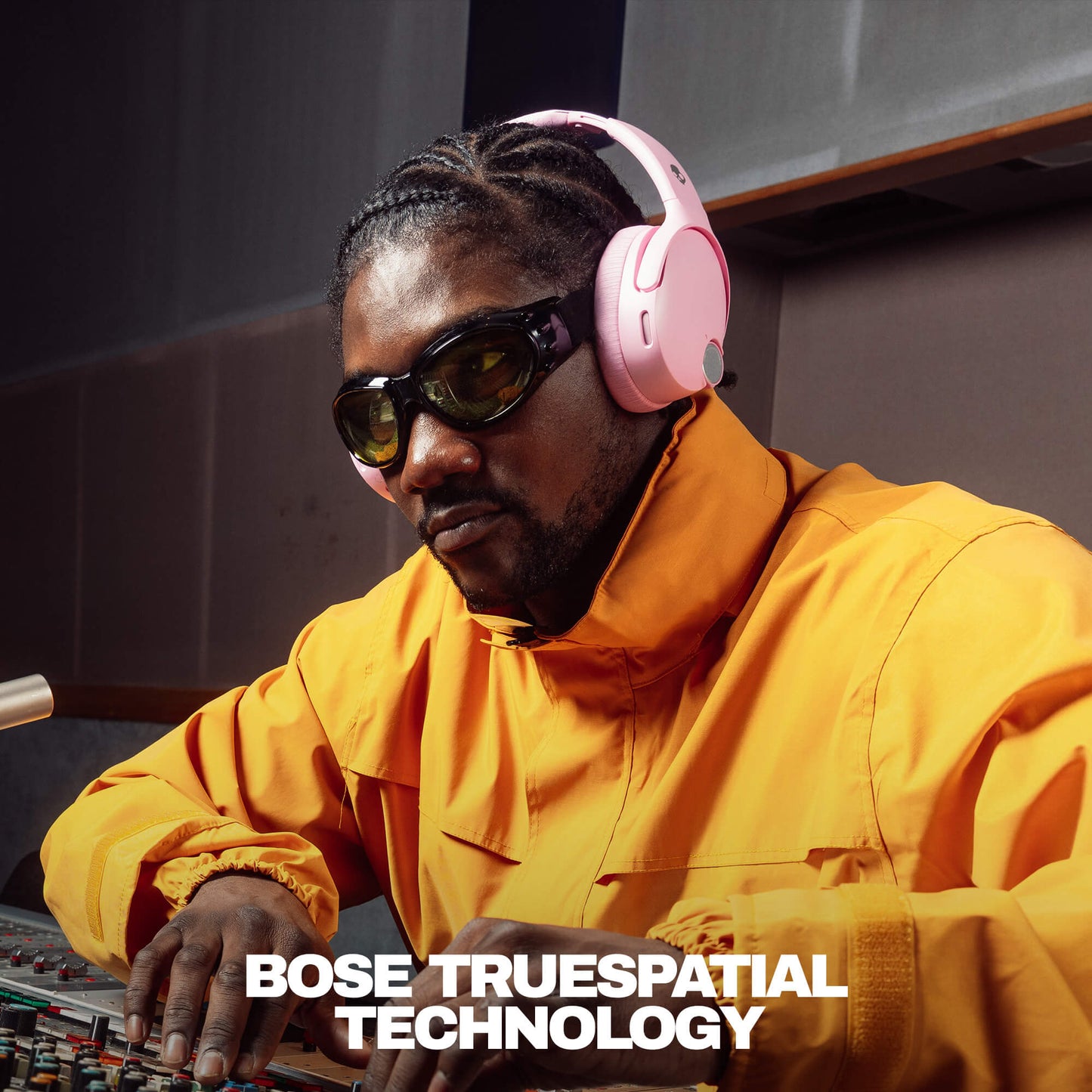 Person wearing pink Crusher 1080 and sunglasses, sitting at a mixing console with 'Bose TrueSpacial Technology' text.  | Candy