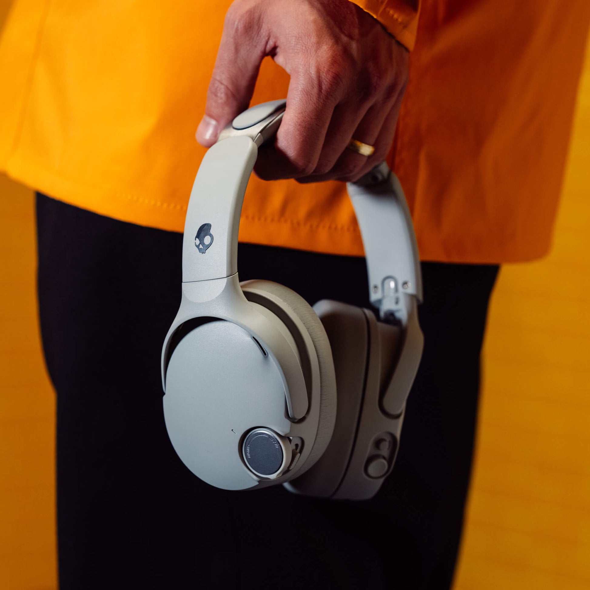 White Crusher 1080 headphones held by a person wearing an orange jacket and black pants. | Cement