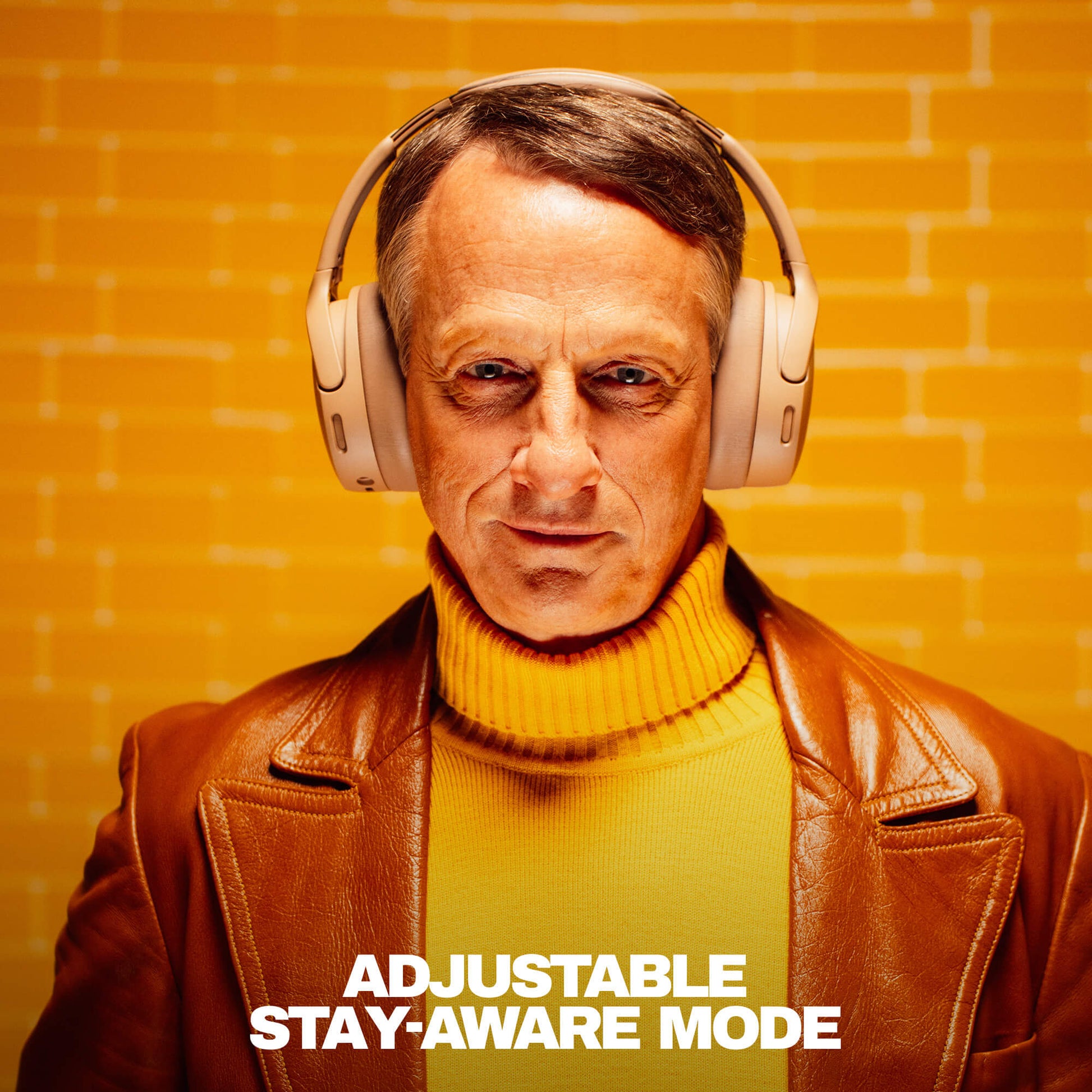 Tony hawk wearing Crusher 1080 headphones with a text 'Adjustable Stay-Aware Mode' on an orange brick wall background | Primer