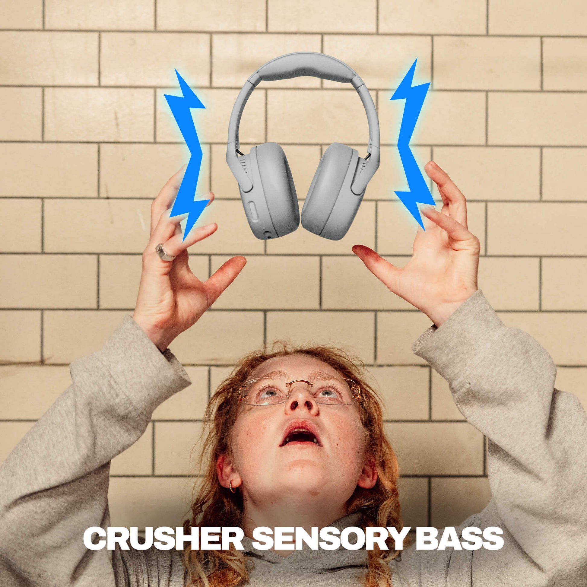 Person holding up Crusher 720 headphones with blue lightning bolts and 'CRUSHER SENSORY BASS' text against a tiled wall. | Cement