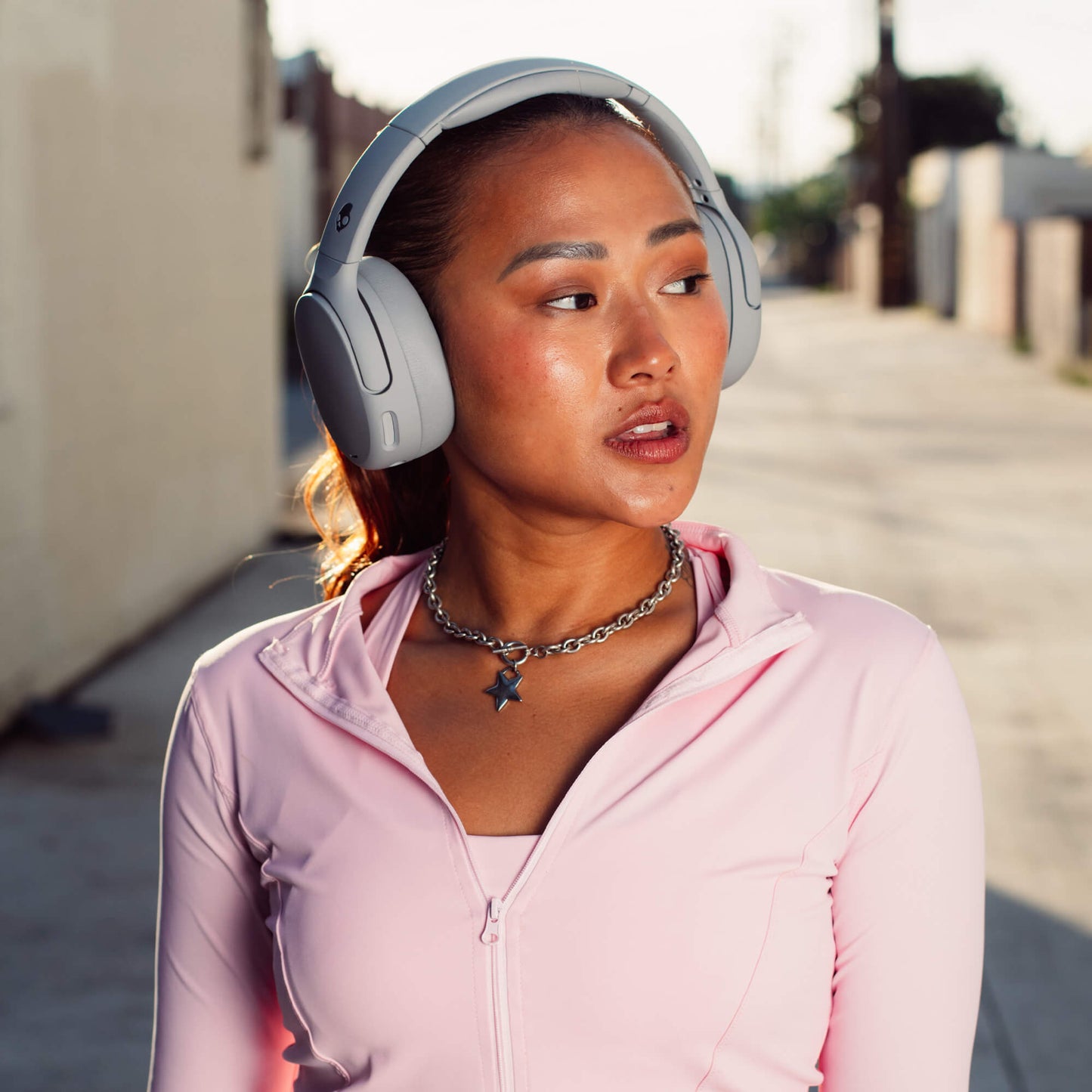 Woman wearing Cruhser 720 headphones and a pink jacket on a street | Cement
