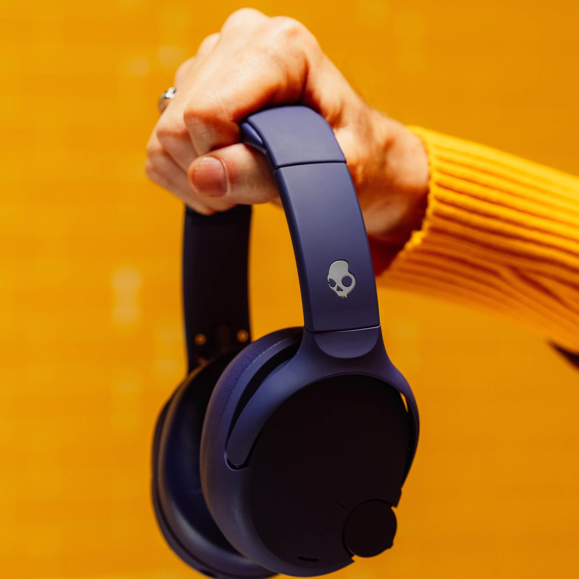 Person holding a pair of blue Crusher 720 with a skull logo against an orange background | Future