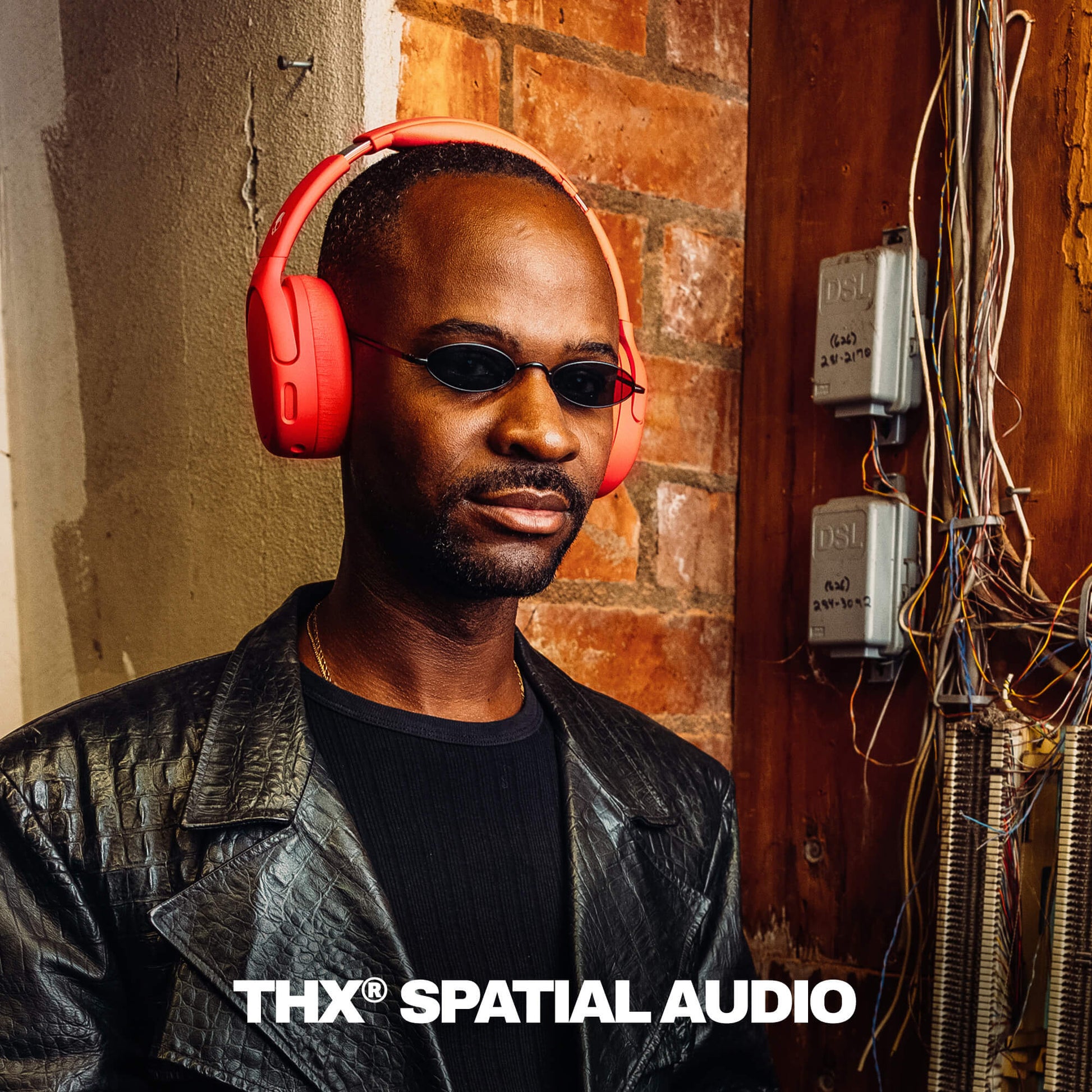 Man wearing red Crusher 720 and sunglasses with 'THX Spatial Audio' branding against a brick wall. | Plasma
