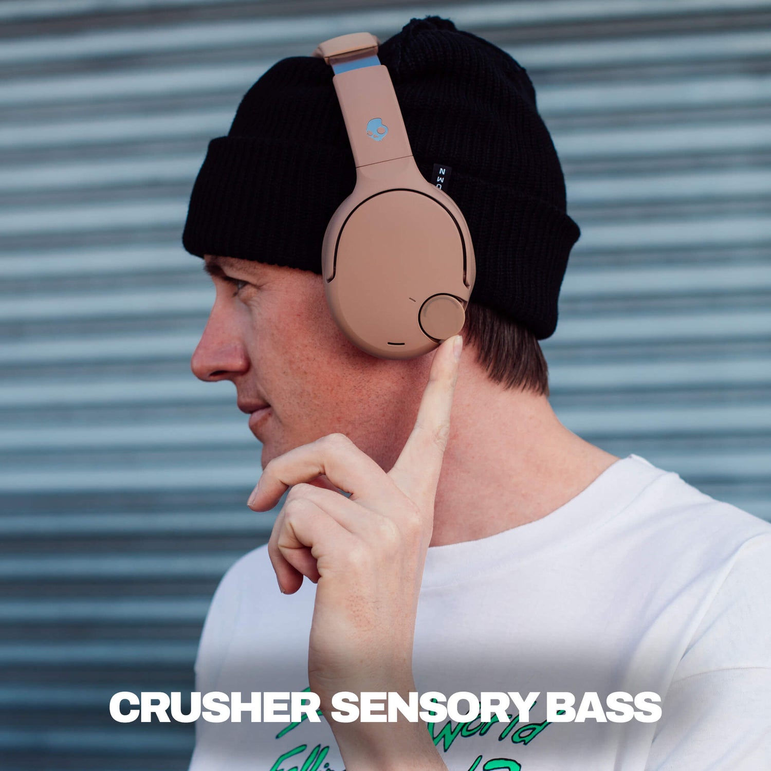 Person wearing a black beanie with brown Crusher 720 headphones, pointing to the headphones, against a metallic background.| Primer