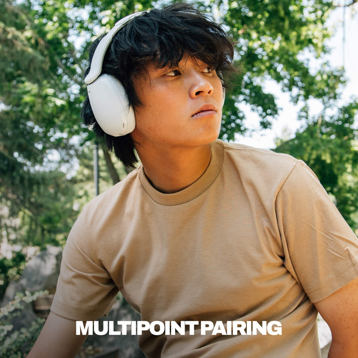 A young man outdoors wearing white hesh 360 over-ear headphones and a beige t-shirt, with the text 'MULTIPOINT PAIRING' overlaid at the bottom. | Bone