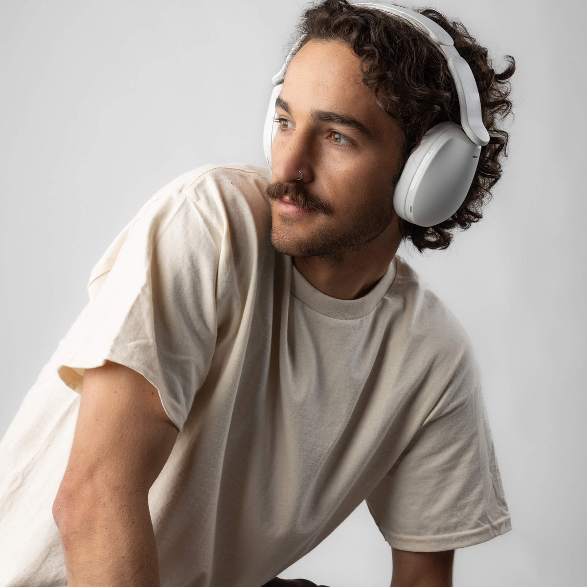 Man wearing white hesh 360 headphones and a beige t-shirt on a light gray background | Bone