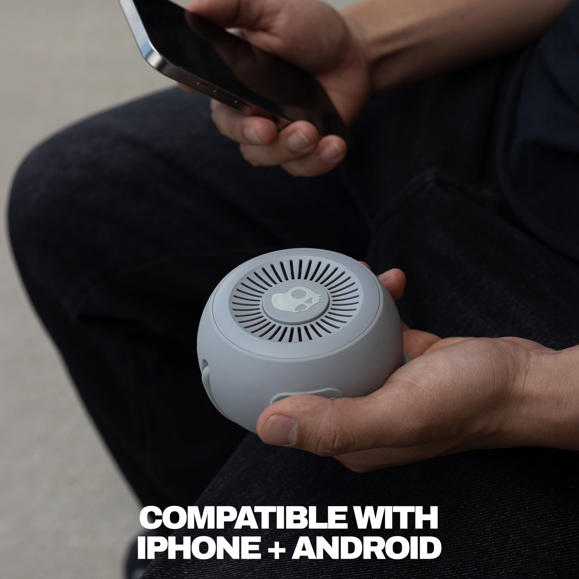 Person holding a small speaker with text indicating compatibility with iPhone and Android. | Cement