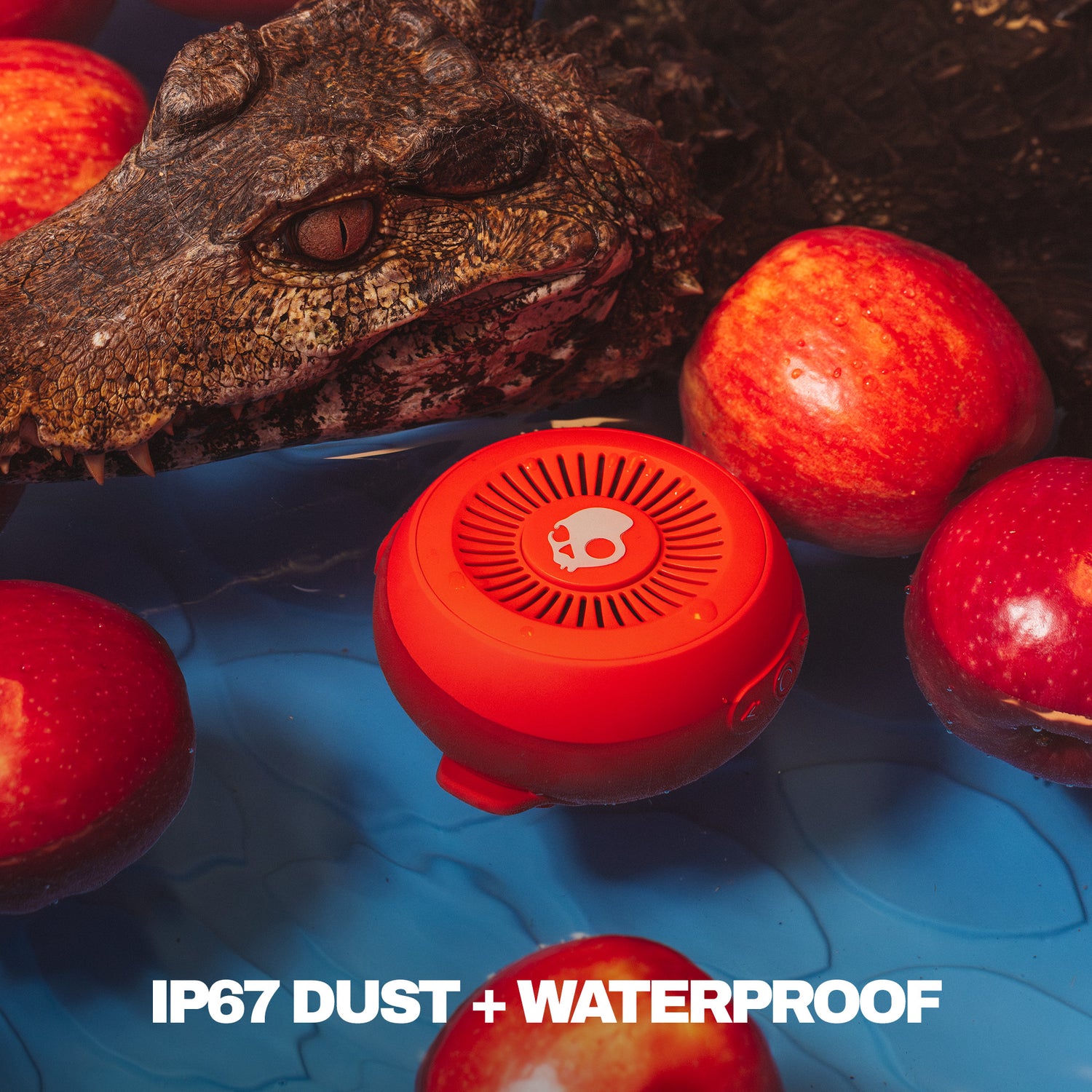 Red waterproof speaker with a crocodile and apples in the background, featuring IP67 dust and waterproof text. | Plasma