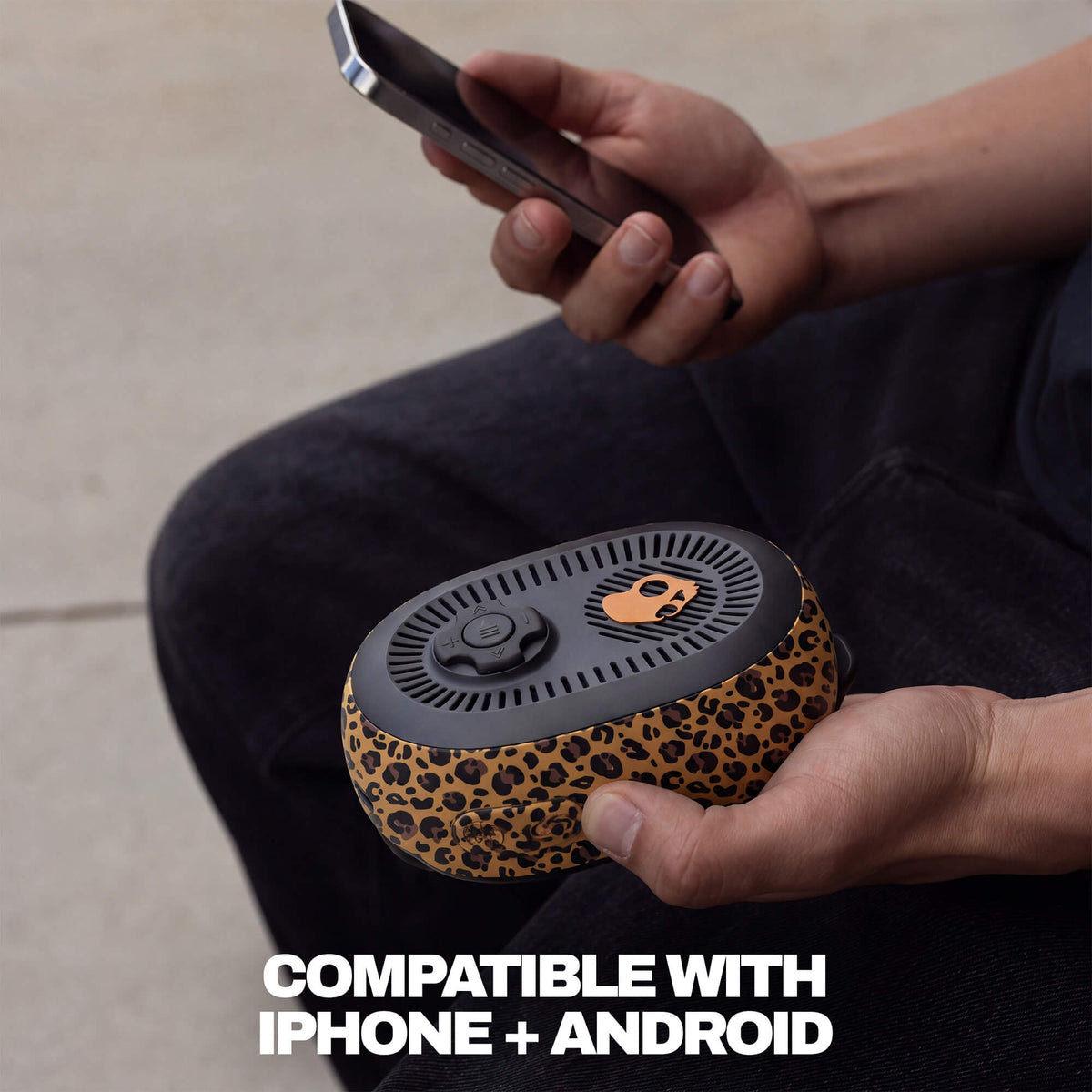 A person holding a leopard-print portable session 540 Bluetooth speaker while using a smartphone, with text at the bottom reading 'COMPATIBLE WITH IPHONE + ANDROID'. | Leopard