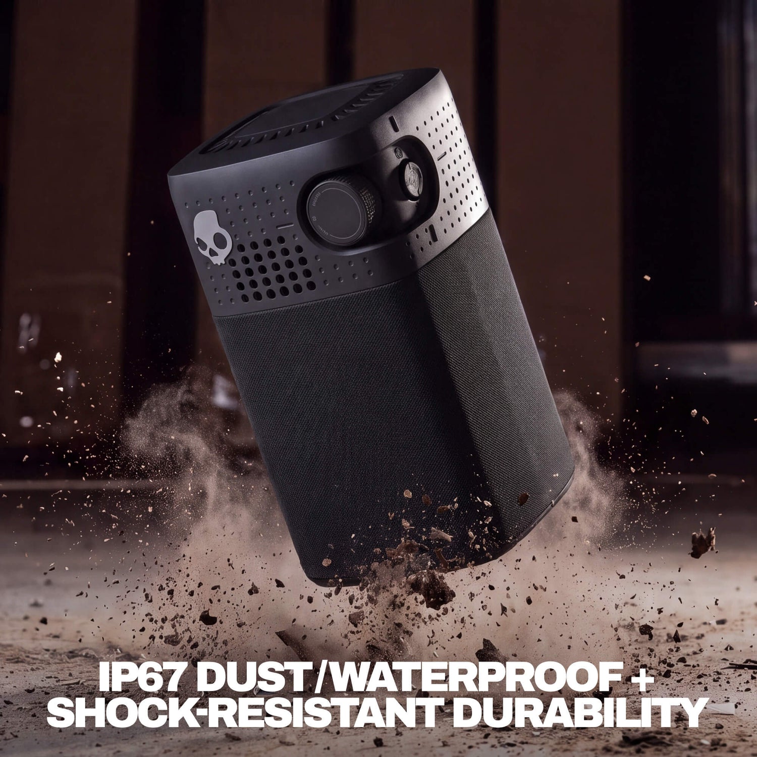 A rugged black session 900 speaker shown floating in midair with dirt and dust splashing around it. The product features a skull logo on the side and bold white text at the bottom reading 'IP67 DUST/WATERPROOF + SHOCK-RESISTANT DURABILITY'. | True Black