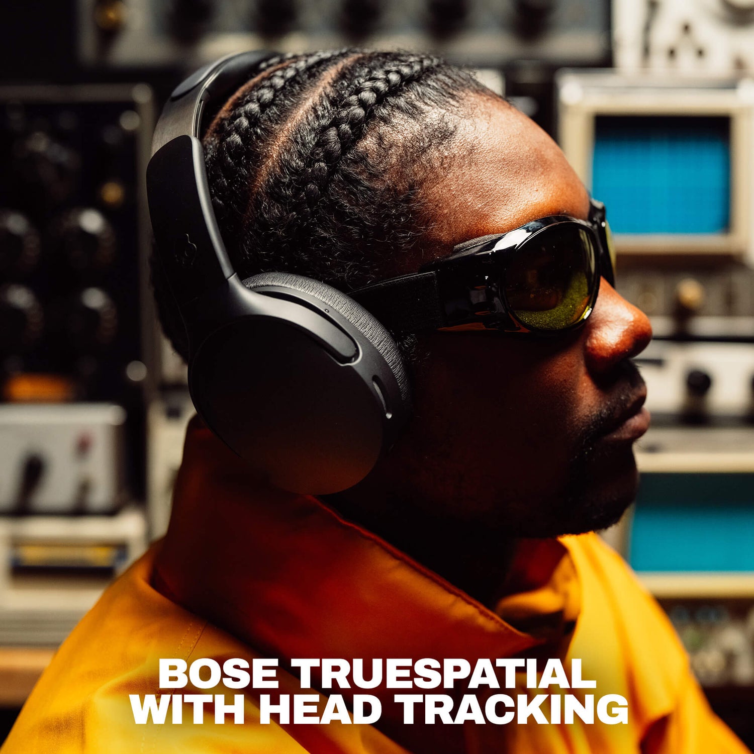 A man in profile wearing black Crusher 1080  headphones with head tracking and dark sunglasses, set against a blurred studio background with audio equipment. White text at the bottom reads 'BOSE TRUESPATIAL WITH HEAD TRACKING'. | True Black