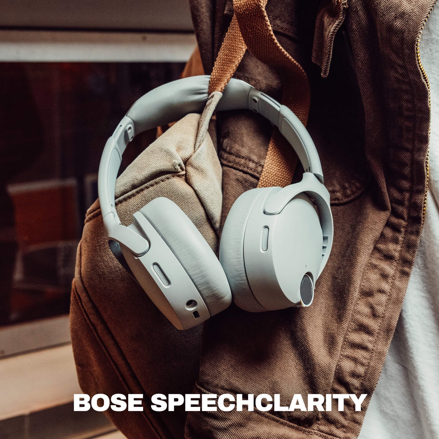 Light gray crusher 1080 over-ear headphones hanging from a brown jacket, with the text 'BOSE SPEECHCLARITY' at the bottom. | Cement